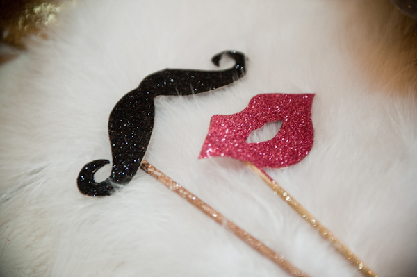 Bride and groom's fun masks sitting on top of white fur - Black sparkly mustache and dark pink sparkly lips - photo by Portland wedding photographer Barbie Hull 